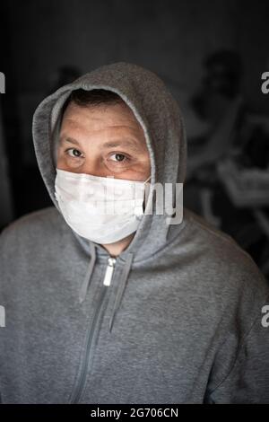 Jeune homme adulte avec un capot gris dans un masque médical. Sans repos, regardez bien droit. Arrière-plan gris foncé. Mise au point sélective. Concept, prévention du vir Banque D'Images