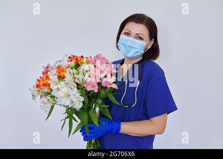 Femelle medic en bleu uniforme masque médical avec bouquet de fleurs sur fond clair Banque D'Images