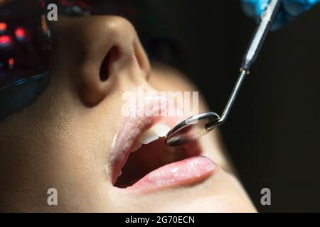 Le dentiste examine et vérifie les dents d'une femme avec un miroir dentaire, vérifie, gros plan. Banque D'Images