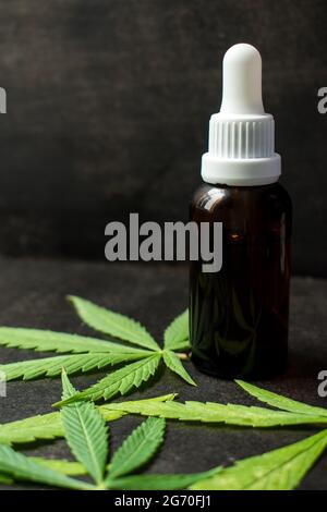 Bouteille de verre brun de compte-gouttes avec quelques feuilles de cannabis sur une table en bois noir avec espace de copie Banque D'Images