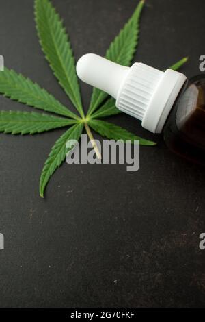 Bouteille de verre brun de compte-gouttes avec quelques feuilles de cannabis sur une table en bois noir avec espace de copie Banque D'Images