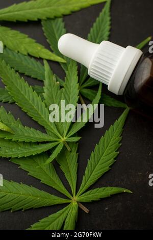 Bouteille de verre brun de compte-gouttes avec quelques feuilles de cannabis sur une table en bois noir avec espace de copie Banque D'Images