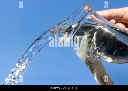 Une eau claire s'écoulant d'une verseuse en verre sur un fond bleu. Banque D'Images