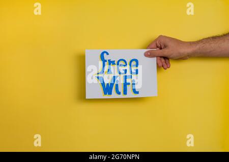 Gros plan d'un homme tenant un papier avec le mot « WIFI GRATUIT » sur fond jaune Banque D'Images