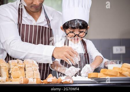 Asian Boy Wear verres tease DAD cuisine avec la farine blanche pétrissage pain pâte enseigne aux enfants la pratique de cuire des ingrédients pain, oeuf sur la vaisselle dans Banque D'Images