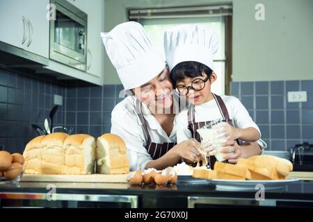 Asian Boy Wear verres tease DAD cuisine avec la farine blanche pétrissage pain pâte enseigne aux enfants la pratique de cuire des ingrédients pain, oeuf sur la vaisselle dans Banque D'Images