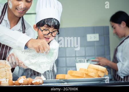 Asian Boy Wear verres tease DAD cuisine avec la farine blanche pétrissage pain pâte enseigne aux enfants la pratique de cuire des ingrédients pain, oeuf sur la vaisselle dans Banque D'Images