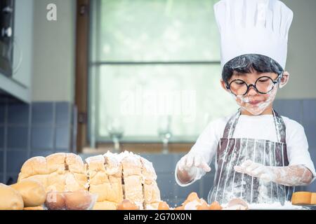 Asian Boy Wear verres tease DAD cuisine avec la farine blanche pétrissage pain pâte enseigne aux enfants la pratique de cuire des ingrédients pain, oeuf sur la vaisselle dans Banque D'Images