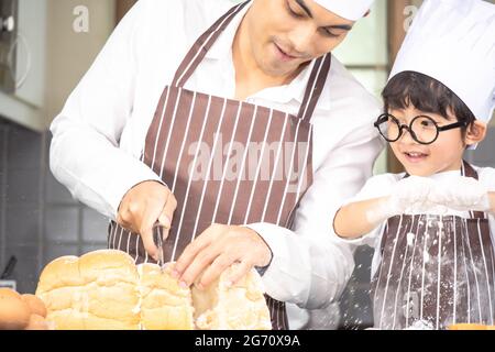 Asian Boy Wear verres tease DAD cuisine avec la farine blanche pétrissage pain pâte enseigne aux enfants la pratique de cuire des ingrédients pain, oeuf sur la vaisselle dans Banque D'Images