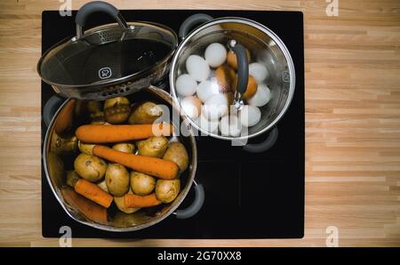 faire bouillir les œufs et les légumes dans des casseroles sur une plaque de cuisson à induction céramique Banque D'Images