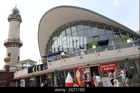 29 juin 2021, Mecklembourg-Poméranie occidentale, Warnemünde : promenade à pied le long de la promenade de la station balnéaire Baltique, après le Teepott, l'un des sites les plus célèbres de la ville. La construction de l'hypercoque par Ulrich Müther a été construite en 1968. Le bâtiment vieillissant a un besoin urgent de rénovation. Sur la gauche se trouve le phare de Warnemünde. Photo: Bernd Wüstneck/dpa-Zentralbild/dpa Banque D'Images