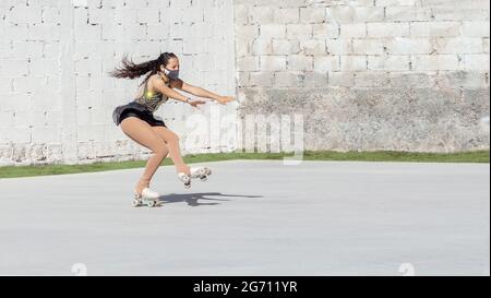 Adolescent latin avec masque, en train de faire du patinage artistique sur roulettes, tombant d'un saut d'axel à l'extérieur Banque D'Images