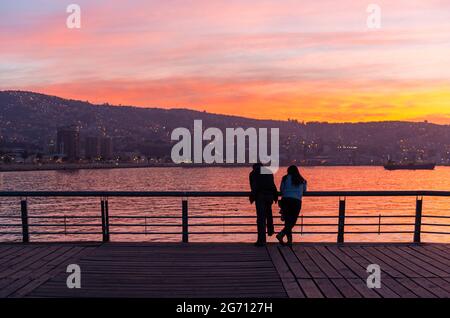 Vue sur Valpraraiso et la baie au bord de l'océan Pacifique avec un couple romantique en premier plan en profitant de la vue au coucher du soleil, au Chili. Banque D'Images