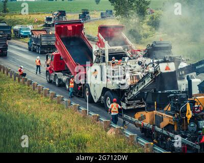 Plusieurs ouvriers avec des casques de sécurité et des gilets orange réfléchissants faisant fonctionner des machines de pavage d'asphalte CAT et des camions à benne basculante sur l'autoroute 25 au Québec. Banque D'Images