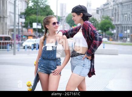 Deux femmes sympa souriant et regardant l'une à l'autre avec un skateboard. Deux amies qui se posent dans la rue. Banque D'Images