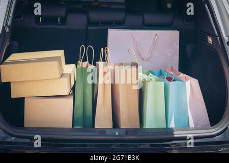 Sacs à provisions entièrement en papier et fourre-tout dans le chariot. Sac coloré et boîte marron dans le coffre de rangement arrière de voiture. Addiction shopping ou concept shopping. Banque D'Images