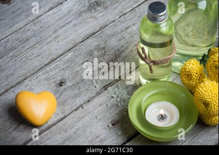 SPA encore vie, coeur jaune, bougie verte allumée, produits de bain, fond en bois Banque D'Images