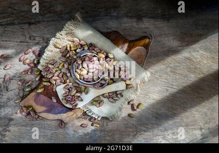 Pile de pistaches décortiquées de noix sur toile de sackCloth sur fond de bois rustique ancien. Graines séchées et fruits mûrs de Pistacia, vue du dessus, espace copie, Banque D'Images