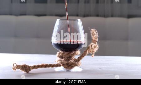 le vin est versé dans le verre est attaché avec une corde. Le concept de dépendance à l'alcool. Banque D'Images