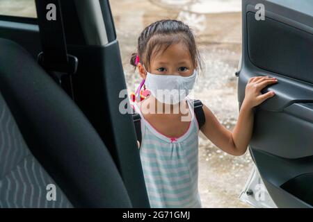 Petite fille asiatique avec masque de visage essayant d'ouvrir la porte d'une voiture. Banque D'Images