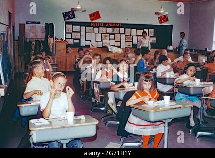 L'éducation en Amérique dans les années 1960 – à l'école primaire Annie Kellond, East Lehigh Drive, Tucson, Arizona, États-Unis en 1969. Ici, les élèves ont une fête de la Saint-Valentin avec de la nourriture et des boissons à leur bureau dans leur salle de classe. Notez les coeurs rouges sur les petits bols en papier, sur les vêtements et attachés aux bureaux. Aux Etats-Unis, la Saint-Valentin (14 février) est devenue un grand événement dans les écoles. À l'école primaire, les enfants échangent des cartes de Saint-Valentin. Cette image provient d'une ancienne transparence couleur amateur Kodak américaine, une photographie vintage des années 1960. Banque D'Images