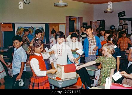 L'éducation en Amérique dans les années 1960 – à l'école primaire Annie Kellond, East Lehigh Drive, Tucson, Arizona, États-Unis en 1969. Ici, les élèves affichent les cartes de Saint-Valentin dans leur salle de classe. Notez les coeurs rouges sur leurs vêtements et attachés aux bureaux. La boîte postale a été adaptée à partir d'une ancienne boîte à chaussures. Aux Etats-Unis, la Saint-Valentin (14 février) est devenue un grand événement dans les écoles. Cette image provient d'une ancienne transparence couleur amateur Kodak américaine, une photographie vintage des années 1960. Banque D'Images