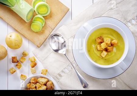 Soupe de poireaux et de pommes de terre avec croûtons. Soupe de légumes maison savoureuse et saine, servie sur une table en bois blanc avec une nappe en lin brodé. À Banque D'Images