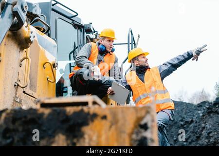 Contremaître montrant le travailleur dans la direction de la fosse minière à ciel ouvert avec ARM étiré Banque D'Images