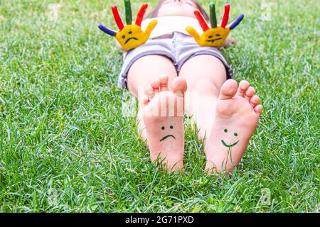 Les pieds de bébé avec le motif de peinture sont souriants et tristes sur l'herbe verte. Mise au point sélective. Banque D'Images