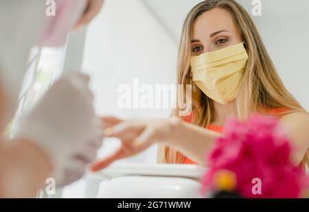 Femme avec masque facial pendant la manucure dans le salon de manucure Banque D'Images
