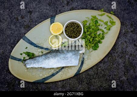 Bar frais pêché au large de la côte de Dorset, sur une assiette ovale en poterie espagnole avec des herbes et du citron frais. Banque D'Images