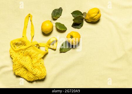 Trois pommes de coing avec feuilles et sac en maille jaune sur fond de lin de couleur pastel froissé. Les fruits biologiques ont des défauts naturels. Une consommation consciente Banque D'Images