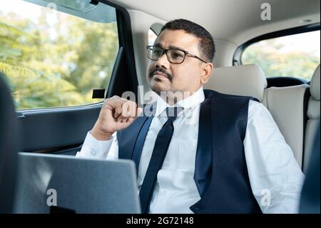 Penser un homme d'affaires sérieux avec un ordinateur portable en voiture ou en taxi - concept de réflexion et d'inquiétude pour le travail et la famille Banque D'Images
