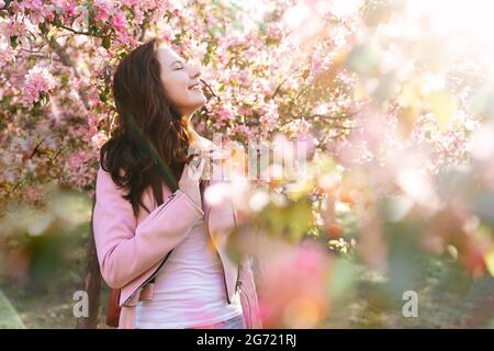 Une jeune femme se tient rêveusement dans un verger de pomme en fleur. Banque D'Images