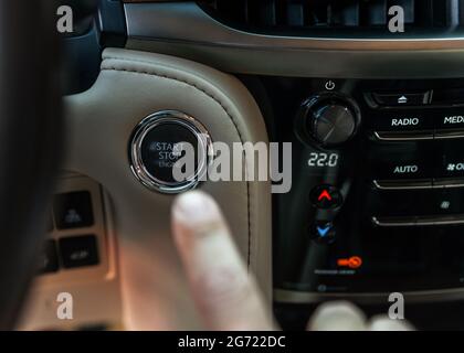 Pression du doigt sur le bouton de démarrage, arrêter le moteur de la voiture de luxe. Le doigt de l'homme appuie vers le bas. Concept du propriétaire et de la concession. Banque D'Images