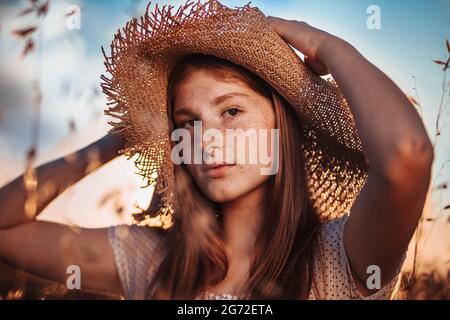 Portrait d'une jeune fille de gingembre, adolescente, avec des taches de rousseur dans le champ de blé portant un chapeau d'été Banque D'Images