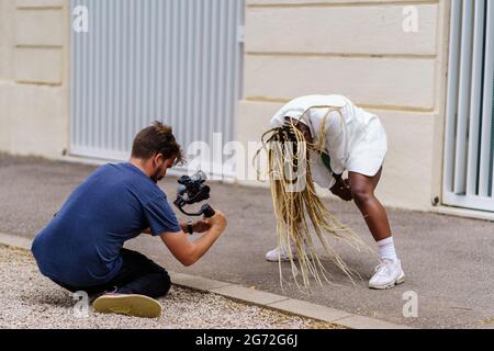 Vidéaste professionnelle au niveau du sol filmant une femme afro-américaine avec sa tête en bas et ses tresses en mouvement. Concept de divertissement, Banque D'Images