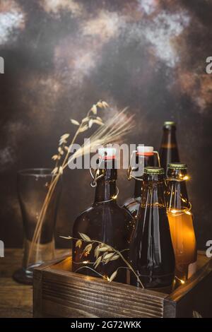 Bannière verticale avec bouteilles de bière froide, maison, claire et sombre, non filtrée, épis de blé dans le verre vide et lumières scintillantes sur un dos brun Banque D'Images