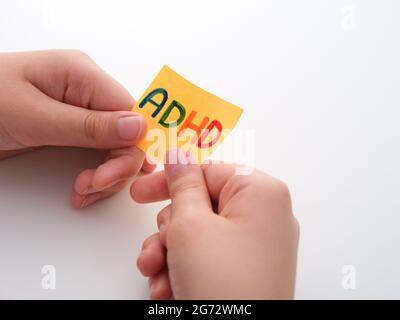 TDAH. Un enfant tenant une note de papier jaune dans ses mains avec l'abréviation TDAH dessus. Gros plan. Le TDAH est un trouble d'hyperactivité avec déficit de l'attention. Banque D'Images