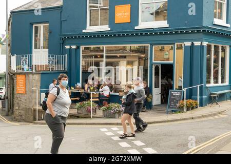 Confortable Cafe Hay on Wye avec des clients assis dehors boire et manger au soleil d'été et les gens qui marchent à côté. Banque D'Images