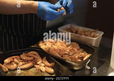 chef épluchant les crevettes avec des gants bleus Banque D'Images