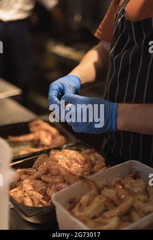 chef épluchant les crevettes avec des gants bleus Banque D'Images