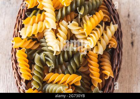 Top vie des pâtes rotini crues de trois couleurs dans un bol en bois Banque D'Images