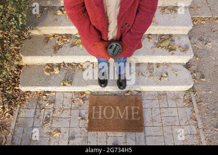 Femme avec une tasse de café près de l'entrée de la maison le jour de l'automne Banque D'Images