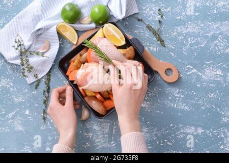 Femme cuisant des pattes de poulet crues sur fond de couleur Banque D'Images