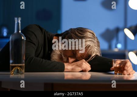Homme âgé inconscient et ivre avec un verre de boisson dans la cuisine la nuit Banque D'Images