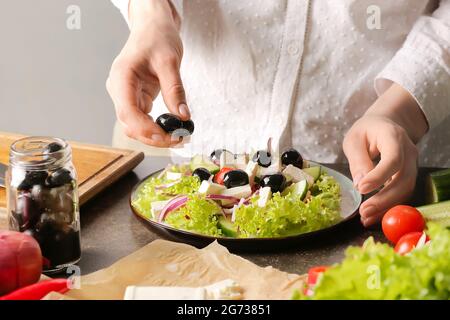 Femme préparant une salade grecque savoureuse sur table Banque D'Images