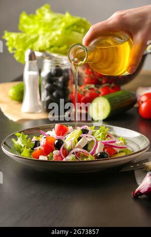 Femme versant l'huile de la bouteille dans l'assiette avec une salade grecque savoureuse sur la table Banque D'Images