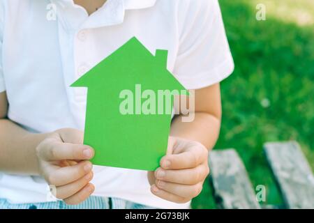 Les mains des enfants tiennent une maison en papier vert. Concept de maisons écologiques Banque D'Images