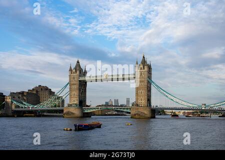 Un petit bateau flotte sur la Tamise en face de l'architecture néo-gothique de Tower Bridge à Londres, en Angleterre. Canary Wharf est vu en bas de la rivière. Banque D'Images